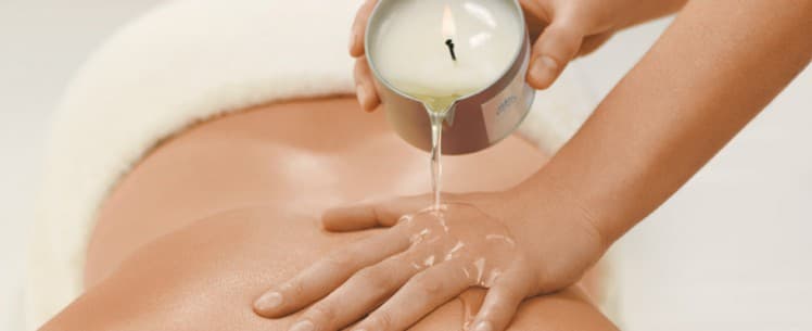 Mãos derramando o o gel que sai das velas corporais sobre o corpo de uma mulher. Um acessório erótico cheiroso e muito sensual.